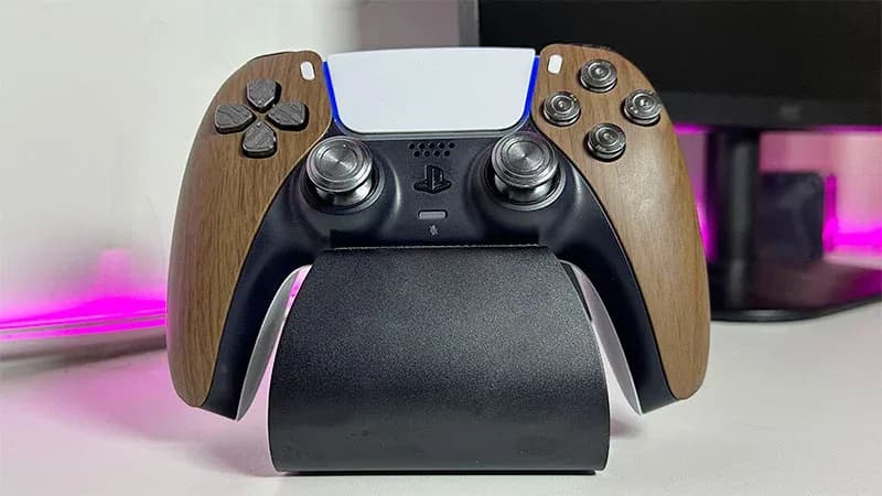 DualSense PS5 tuneado con acabado madera y soporte de carga negro, con luz LED rosa de fondo.