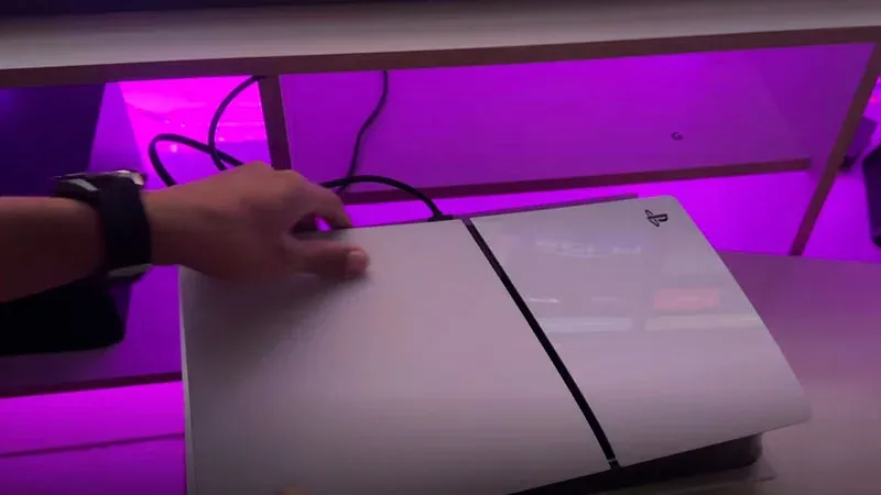 PS5 Slim en posición horizontal sobre una superficie, con iluminación LED morada de fondo.