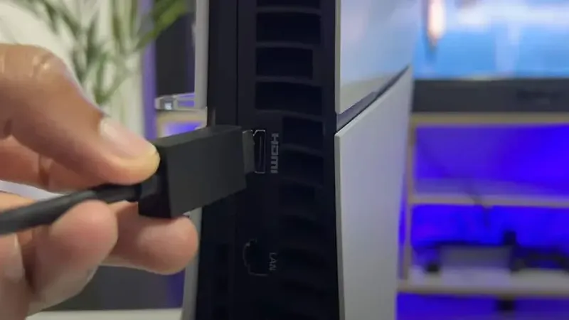 Mano conectando cable HDMI en el puerto trasero de una PS5 Slim con iluminación azul de fondo