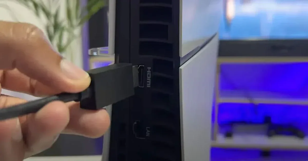 Mano conectando cable HDMI en el puerto trasero de una PS5 Slim con iluminación azul de fondo