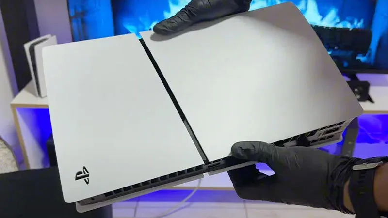 Manos con guantes negros sosteniendo una PS5 blanca abierta para limpieza, mostrando las placas laterales separadas.