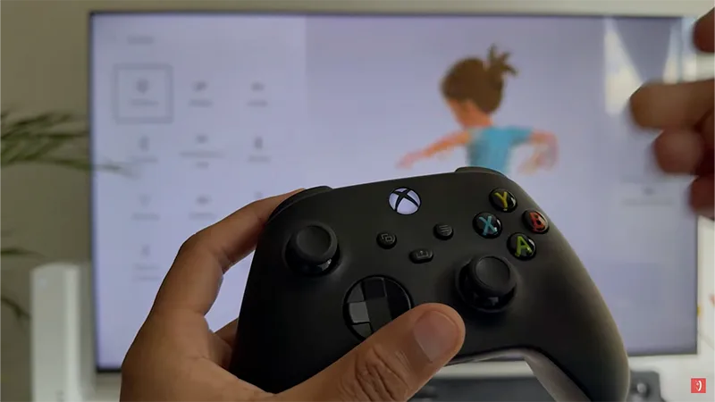 Mando inalámbrico Xbox Series negro sostenido frente a una pantalla con menú de videojuego animado.
