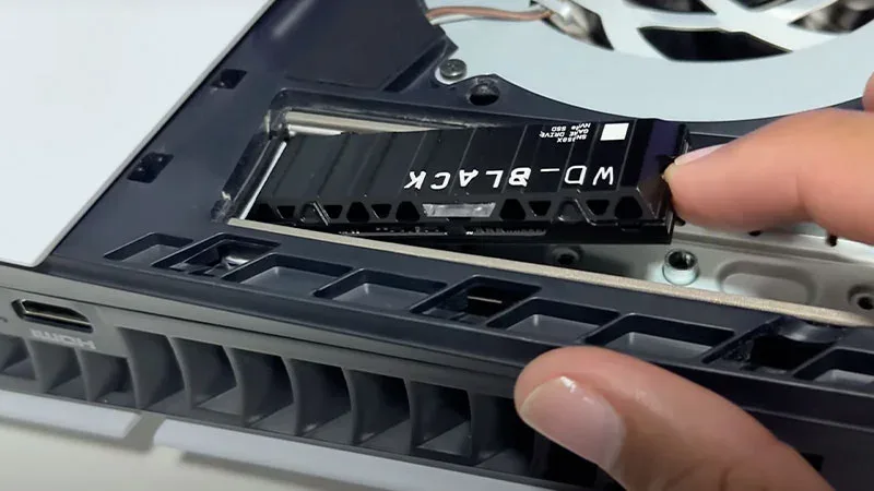 Instalación de SSD NVMe WD_BLACK en ranura M.2 de PS5 Slim con mano sujetando la unidad