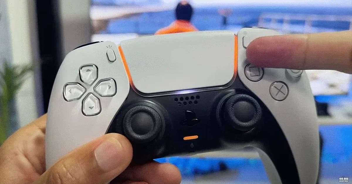 Mando DualSense de PS5 con luz naranja en mano, mostrando botones táctiles, cruceta y joysticks