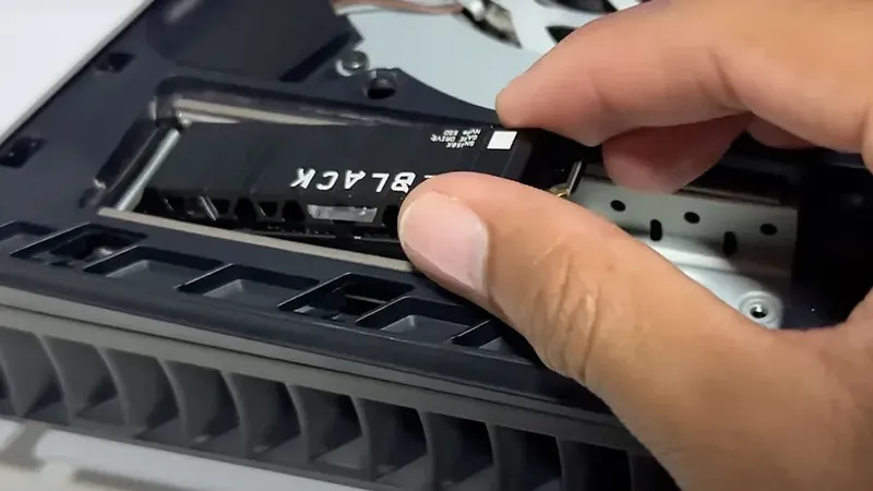 Instalación de SSD WD Black NVMe en ranura M.2 de PS5, mano insertando la unidad en la consola abierta.