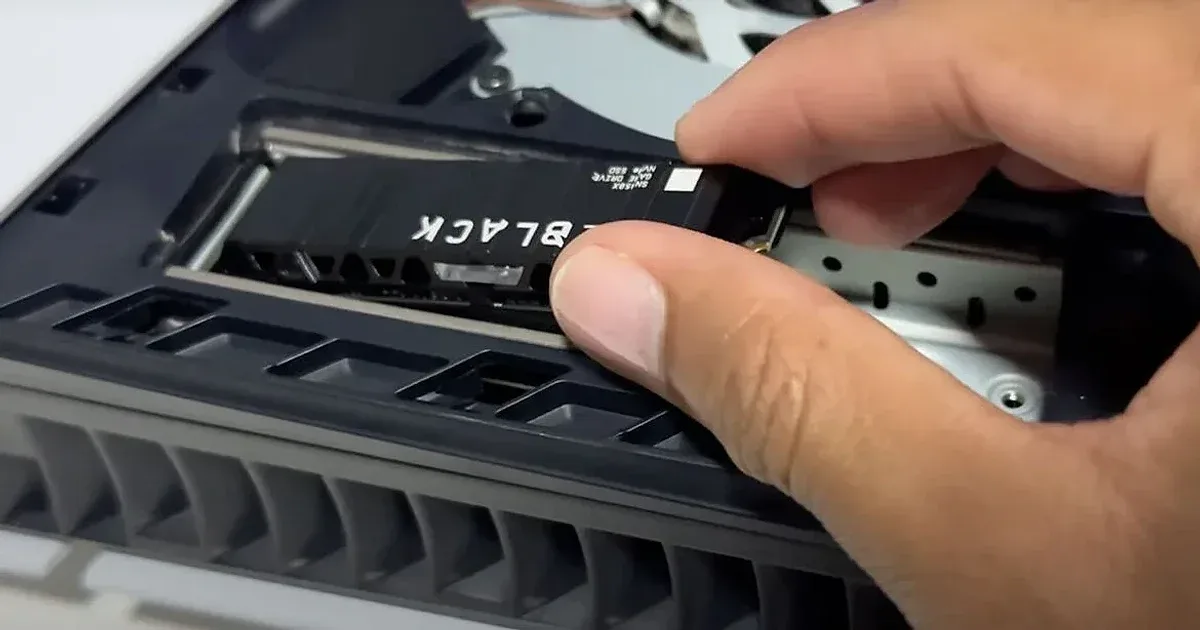 Instalación de SSD WD Black NVMe en ranura M.2 de PS5, mano insertando la unidad en la consola abierta.