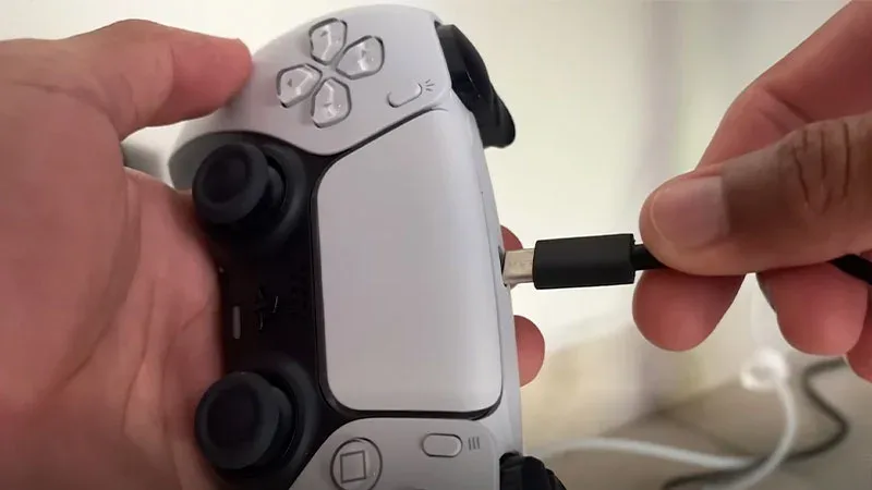 Manos conectando cable USB-C al mando DualSense blanco de PS5 para cargarlo correctamente
