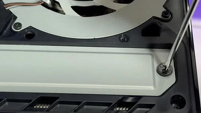 Interior de PS5 mostrando la ranura SSD con tornillo siendo ajustado junto al ventilador de la consola.