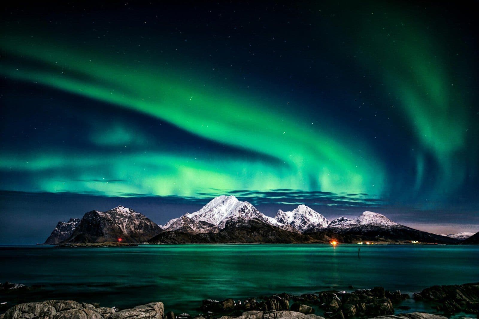 Aurora boreal verde sobre montañas nevadas y lago ártico en paisaje nocturno invernal