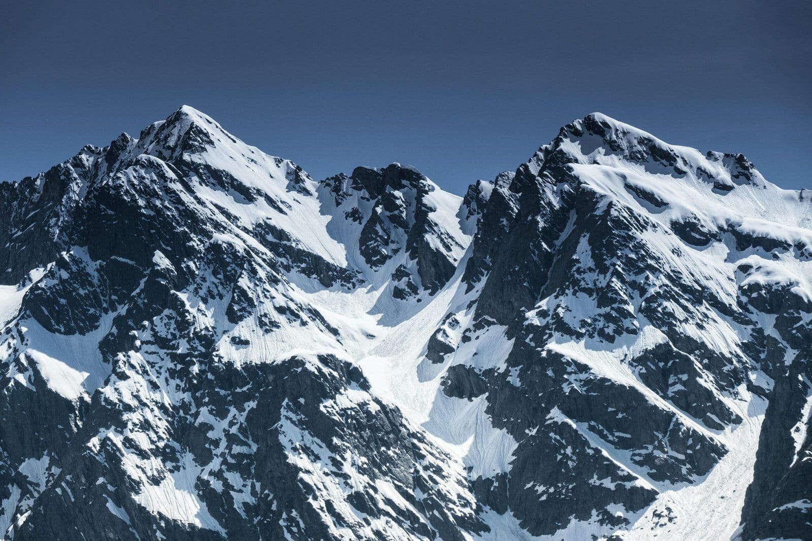 Dos imponentes cumbres nevadas bajo cielo azul despejado, paisaje alpino de montaña en invierno