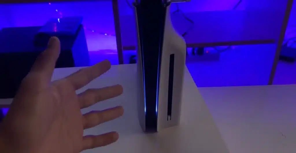 Mano acercándose a una PS5 con luz azul para revisarla cuando la consola no enciende
